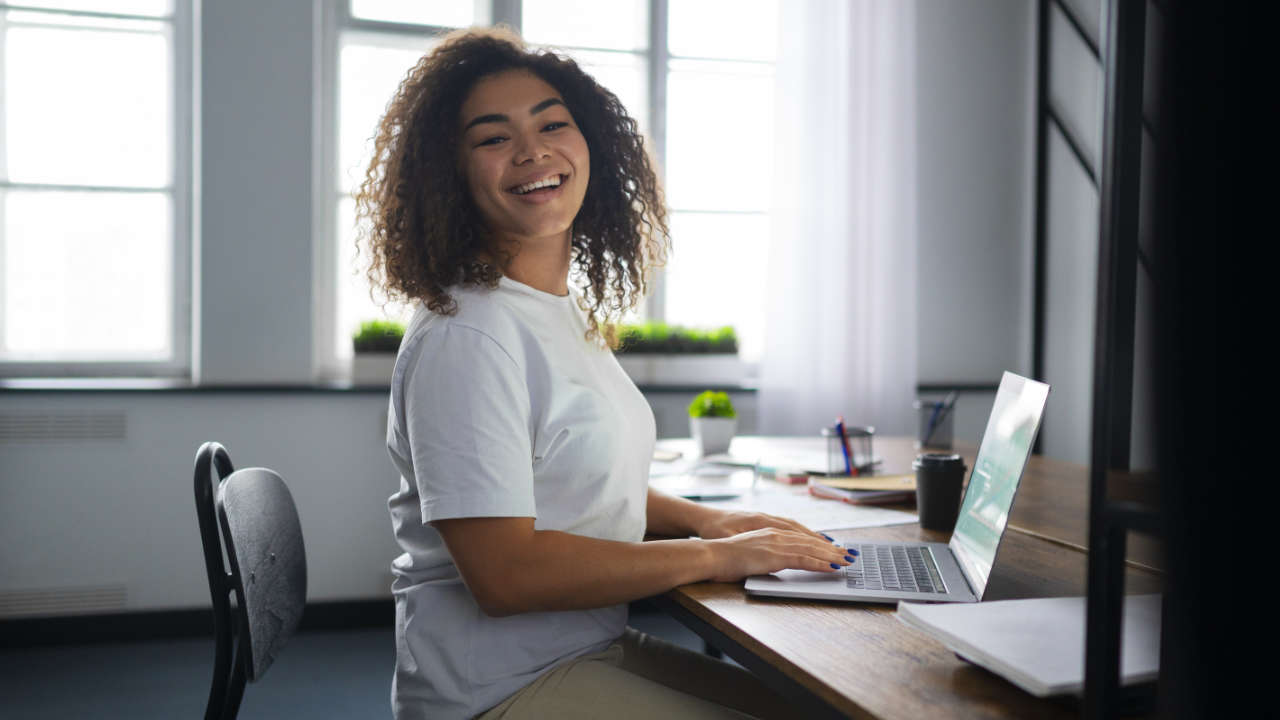 Mulher sorrindo em frente ao notebook enquanto faz inscrição Prouni 2025