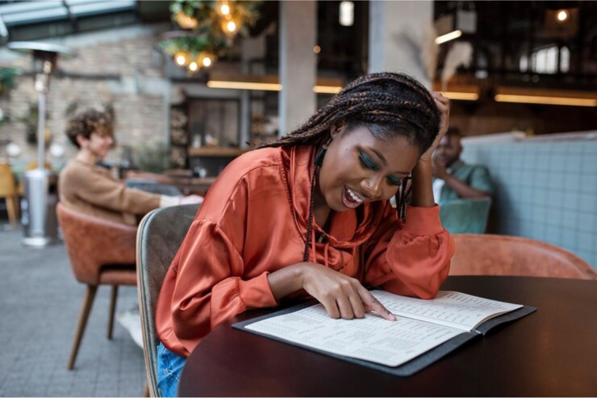 Uma estudante no meio de uma praça de alimentação lê um caderno