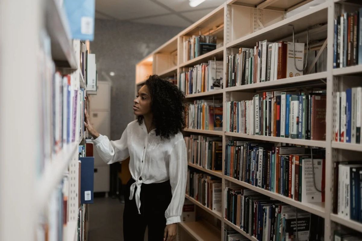 Uma aluna no corredor da biblioteca escolhendo um livro. Ela se prepara para a Inscrição Unip 2025