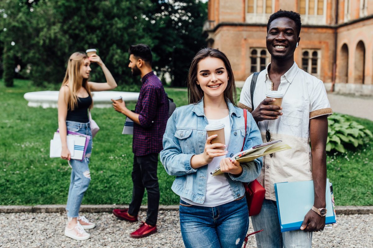 Estudantes com cadernos e copos de café nas mãos no campus de uma instituição de ensino