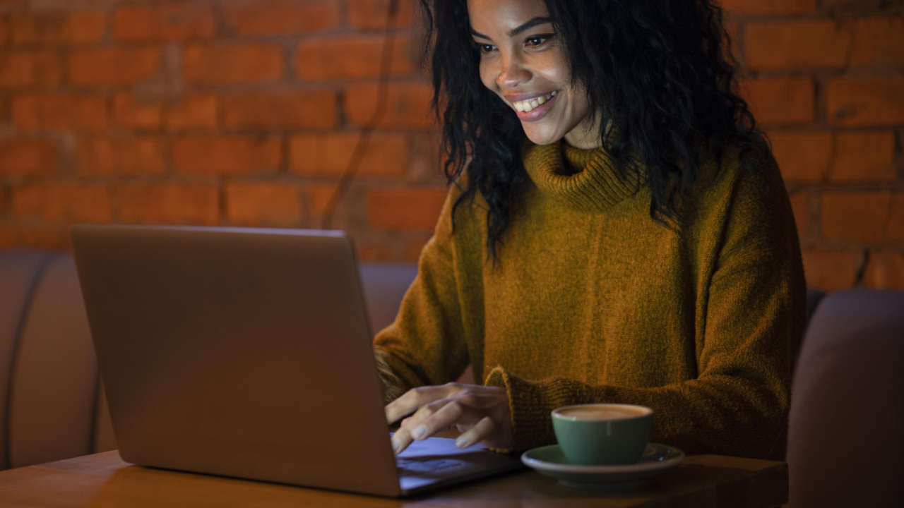 Mulher sentada no sofá usando notebook para fazer inscrição Banrisul 2025