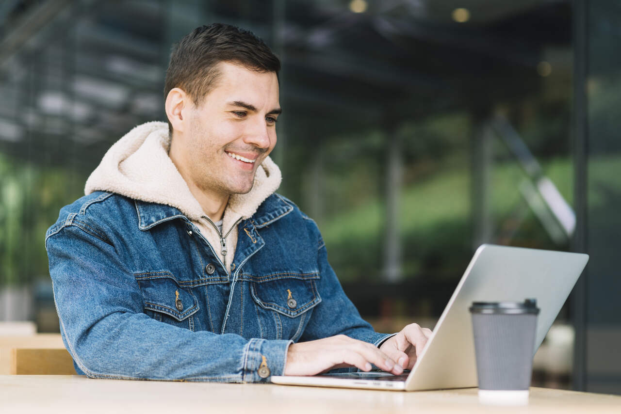 Jovem sorri enquanto trabalha em seu notebook 