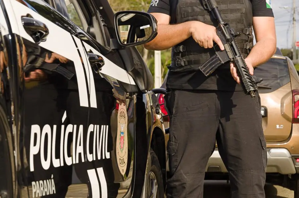 Policial civil do Paraná ao lado de carro oficial portando uma metralhadora 