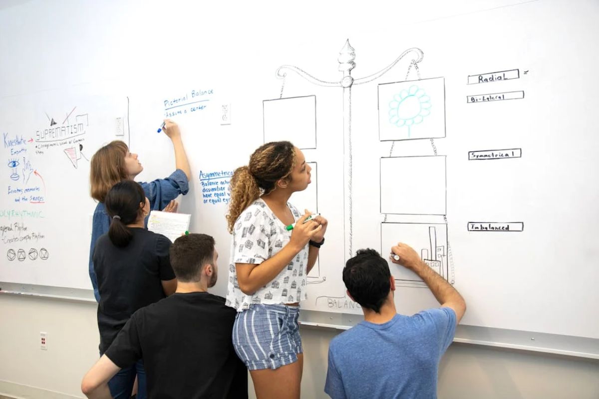 Um grupo de alunos na sala de aula após a Inscrição UP 2025. Eles escrevem em um quadro branco com caneta preta