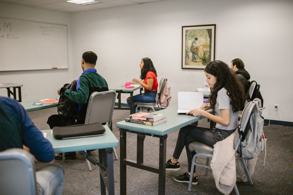 Alguns estudantes sentados dentro da sala de aula em suas cadeiras enquanto estudam