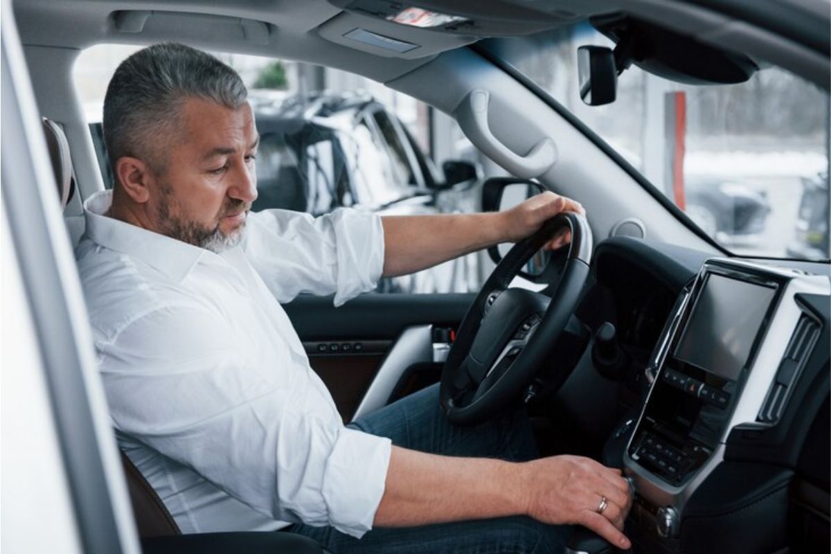 Um motorista com a mão no volante e a outra no rádio, saindo da concessionária 