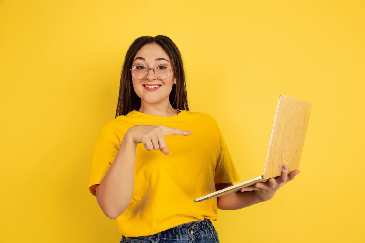 jovem sorridente aponta para notebook aberto em sua mão 