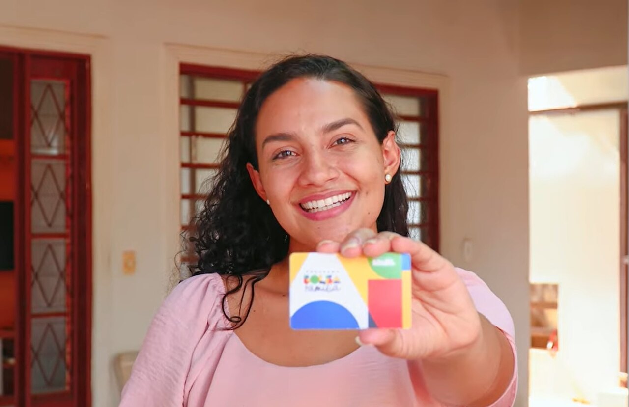 Mulher posa sorridente mostrando seu cartão do Bolsa Família 