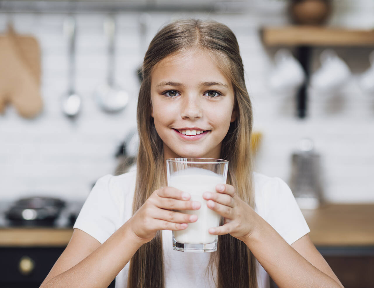 Menina posa sorridente segurando um copo de leite 